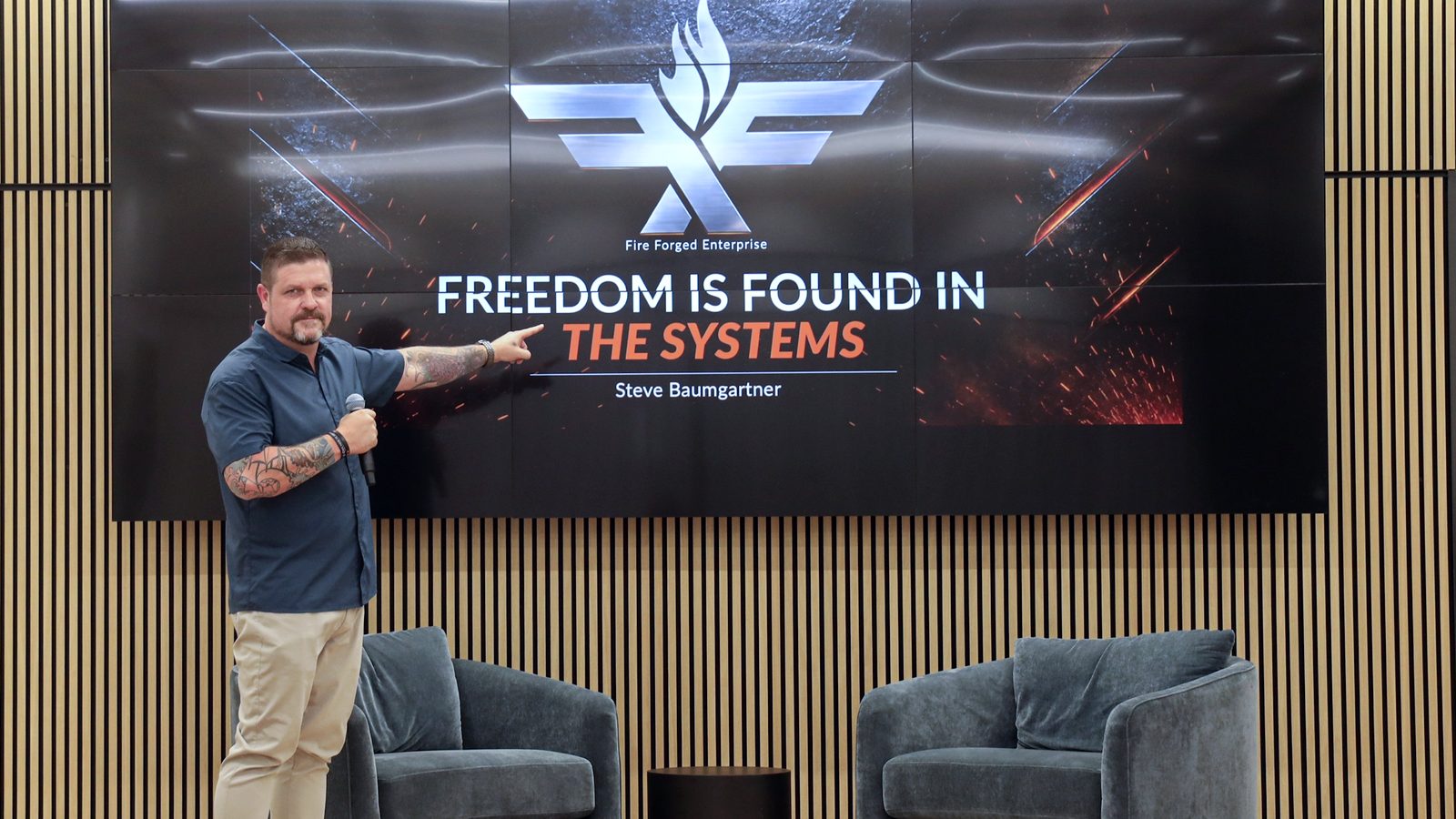 Steve Baumgartner on stage pointing to a slide that reads Freedom is found in the systems